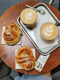 Overhead view of two lattes with heart latte art and two cinnamon buns on a round wooden table