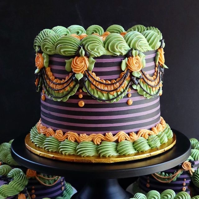 Tall decorated layer cake with green frosting swirls and purple striped sides on a cake stand