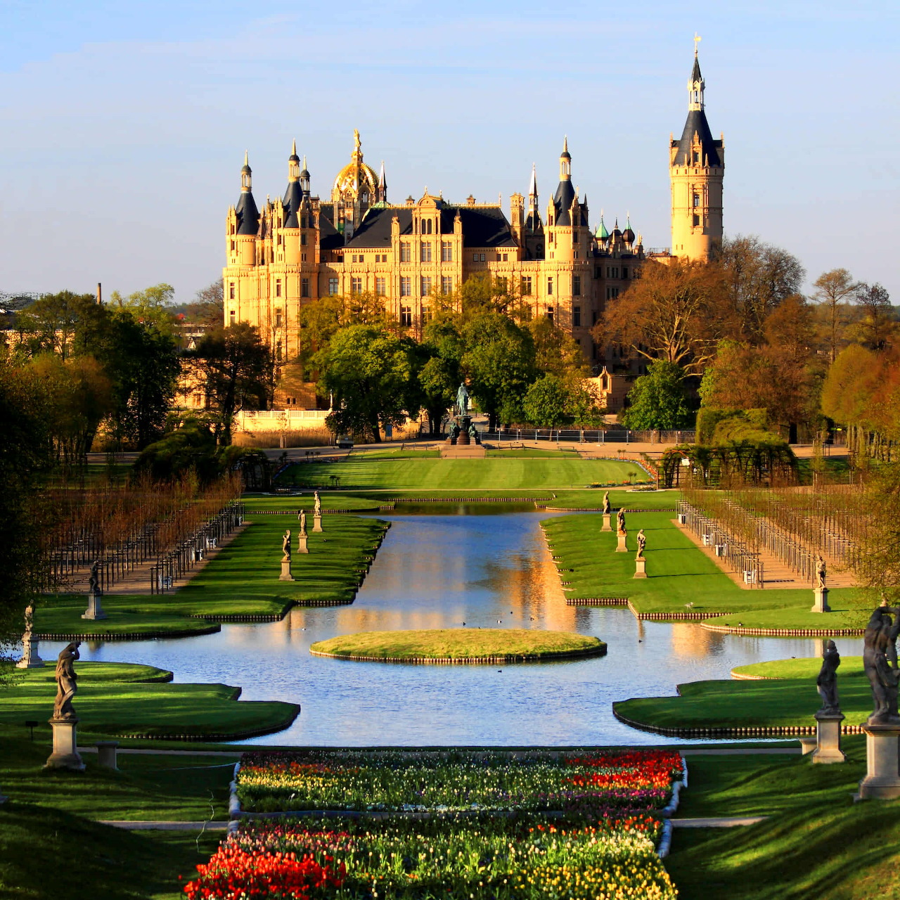 Ornate castle with towers and domes behind formal garden with reflecting pool and green lawns