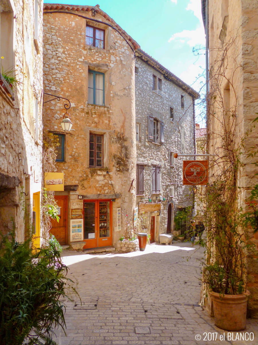 Sunlit cobblestone alley between old stone buildings in a French village with blue sky overhead