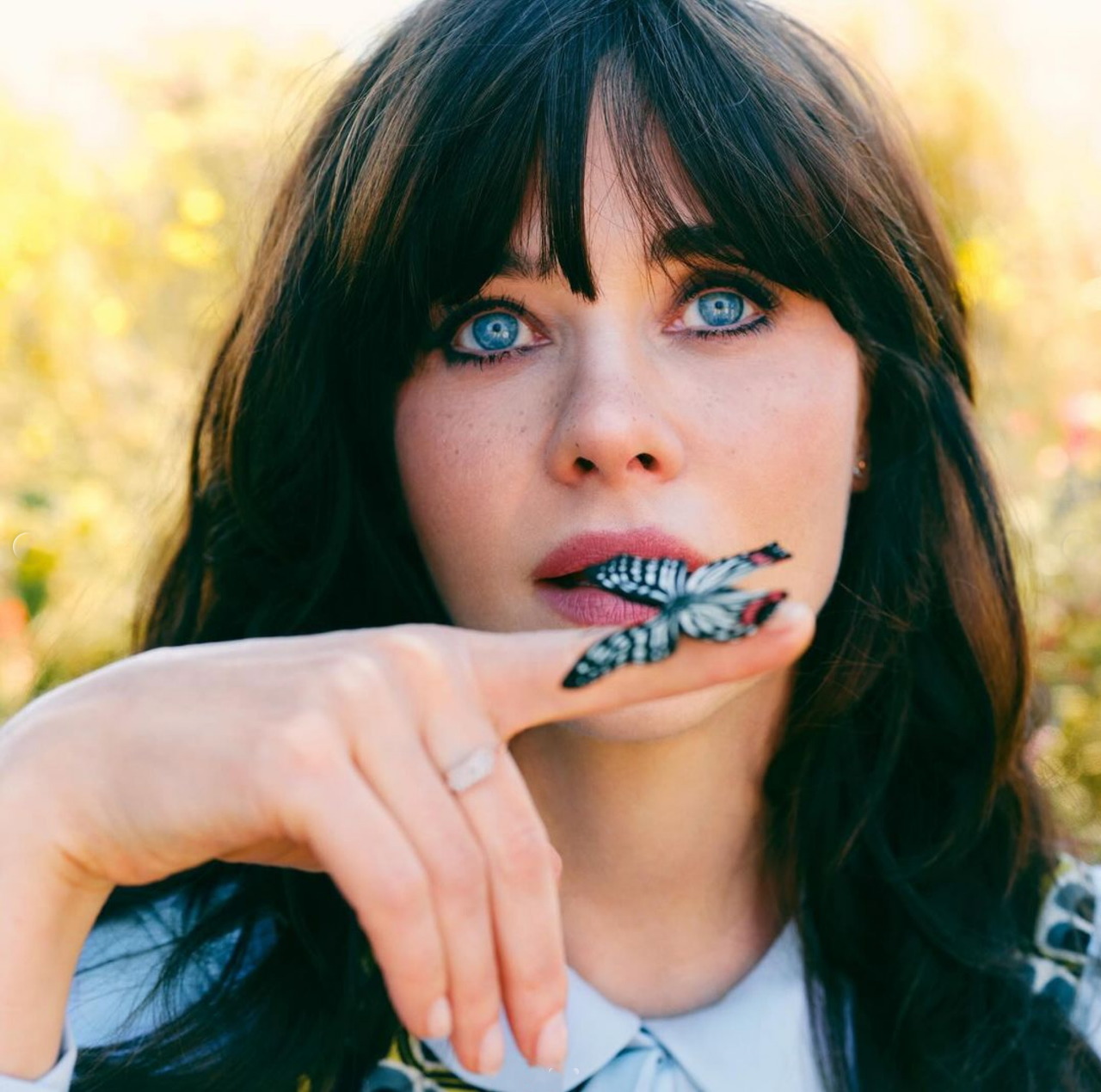 Close-up of Zooey Deschanel holding a butterfly near her lips outdoors