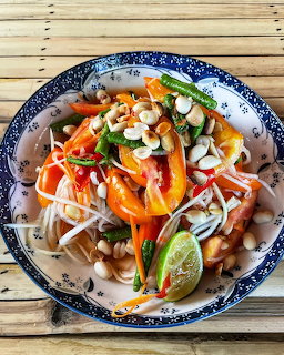 Thai papaya salad with peanuts, lime, and vegetables in a blue patterned bowl on a bamboo mat