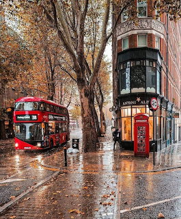 Red London bus on rainy street with autumn trees and Victorian building