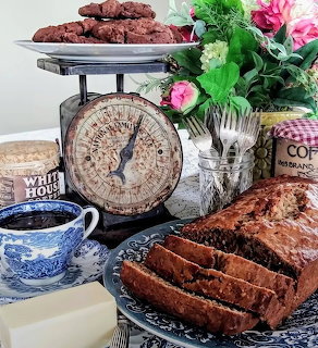 Vintage kitchen scale with banana bread, cookies, teacup and pink flowers on counter