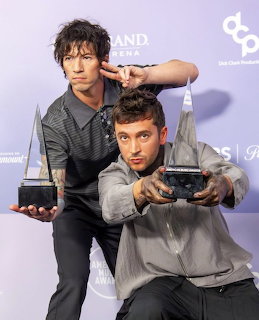 Two men posing with trophy awards at an indoor event backdrop