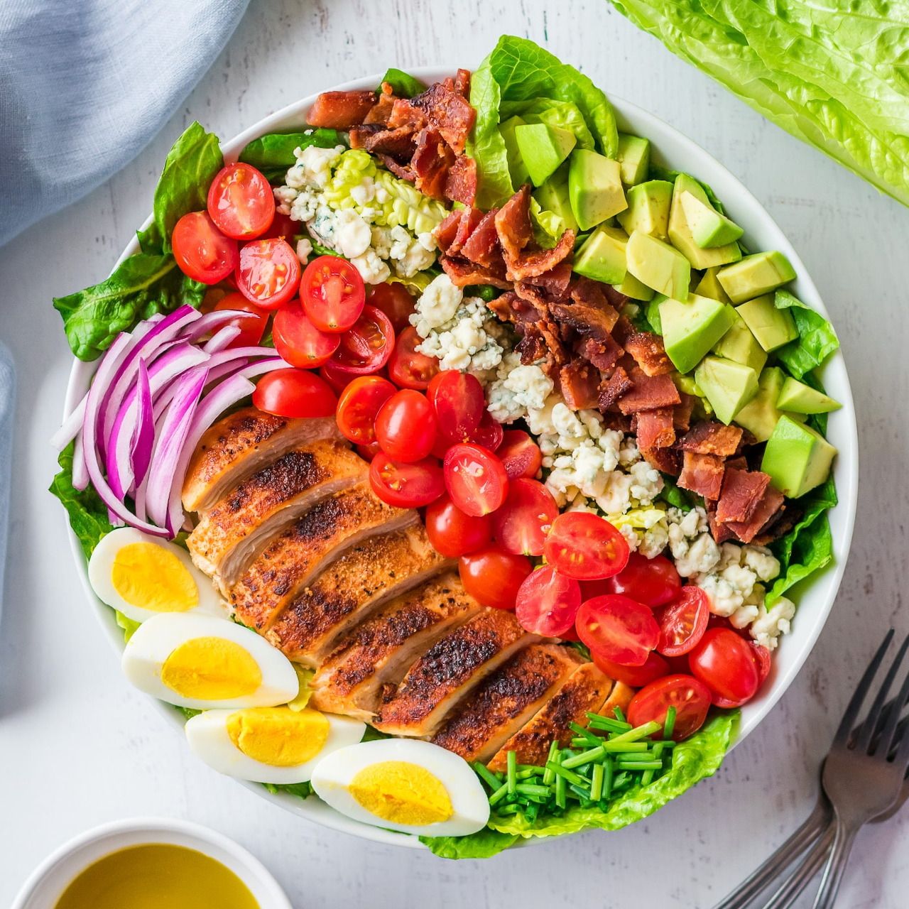 Overhead bowl of Cobb salad with chicken, bacon, avocado, tomatoes, eggs, onion, blue cheese, and lettuce