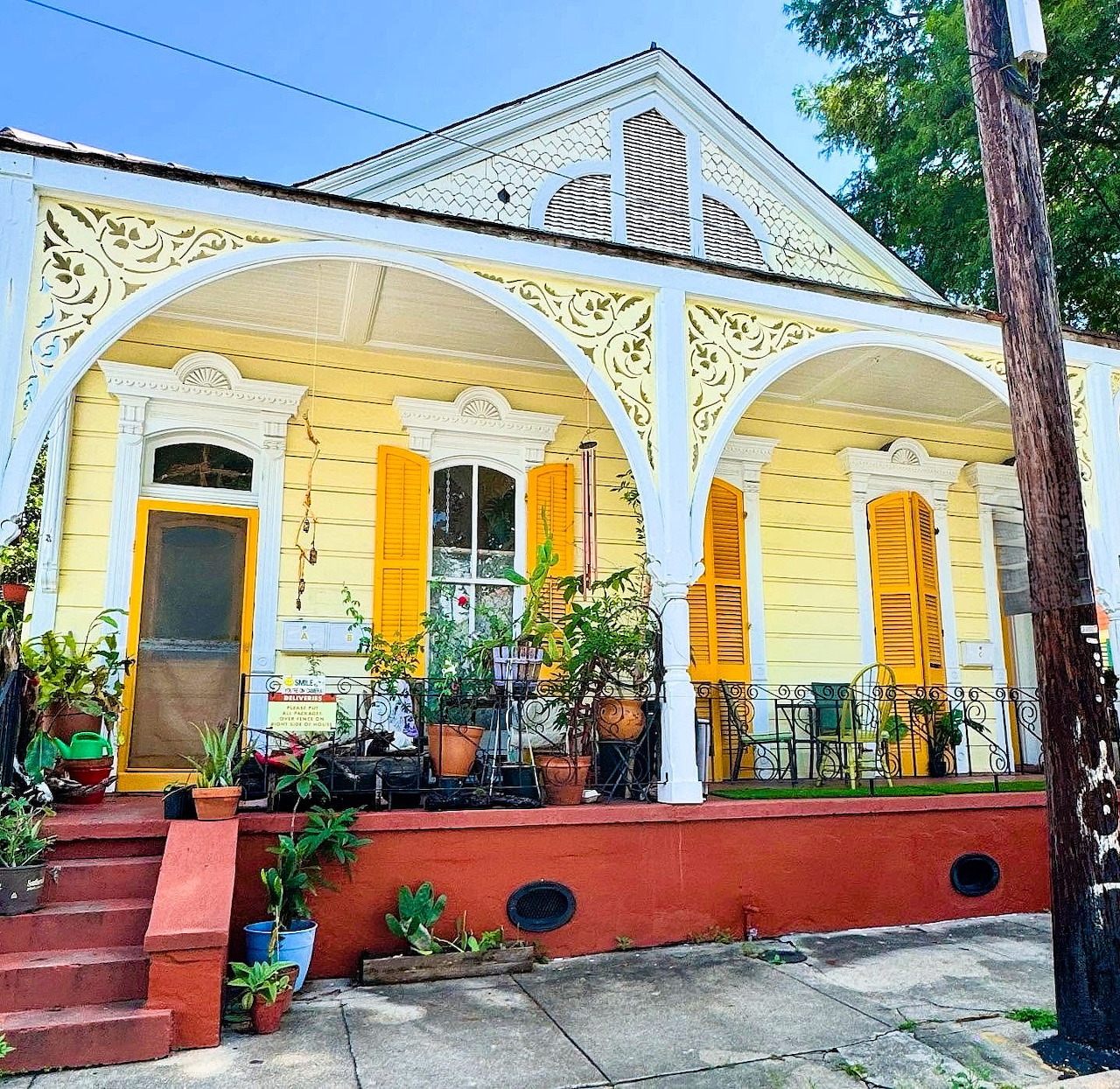Yellow cottage with decorative white porch, potted plants on red steps