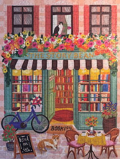 Illustration of a colorful bookstore front with flowers, a blue bicycle, cafe chairs, and a cat