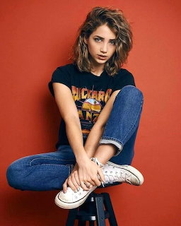 Young woman sitting on a stool in jeans and a graphic T-shirt against an orange backdrop