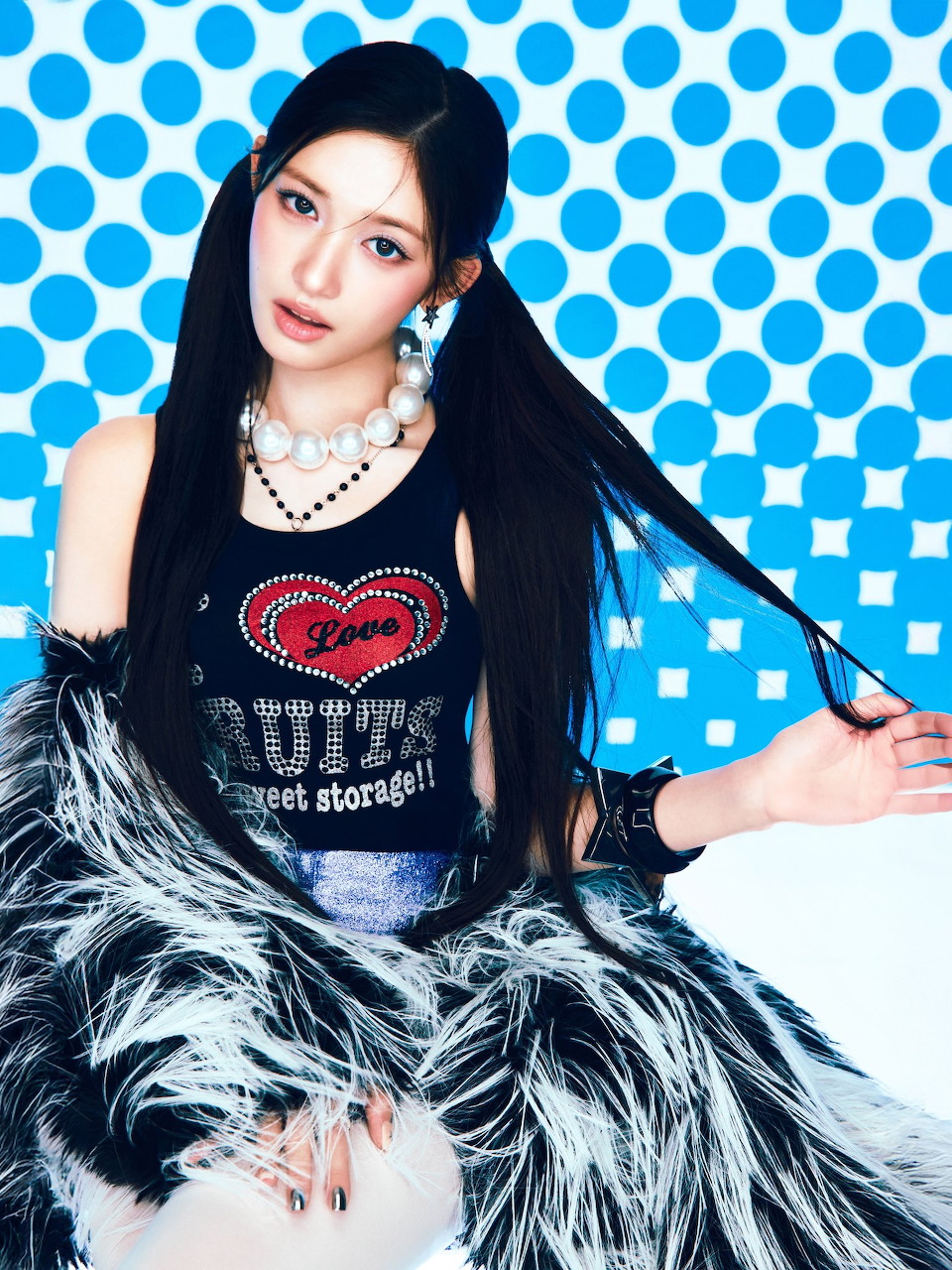 Young woman with long black hair in graphic tank top and feathered jacket, blue polka dot background