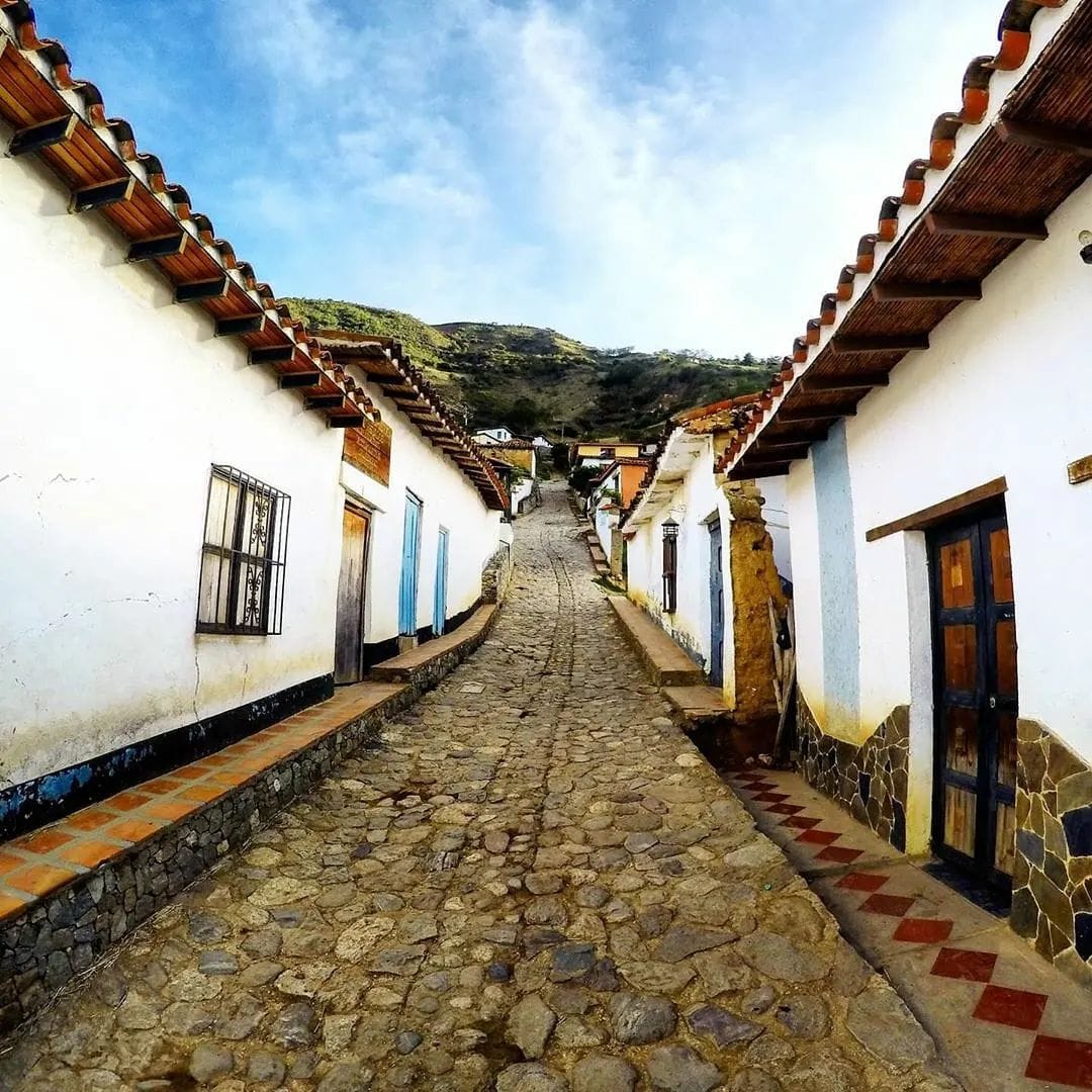 Narrow cobblestone street between white colonial houses with red tile roofs in a mountain village