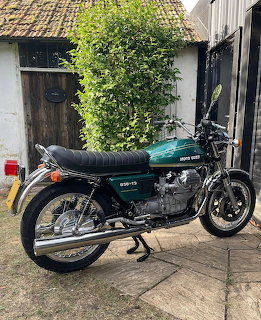 Green Moto Guzzi 850 T3 vintage motorcycle parked outside a white cottage with tiled roof