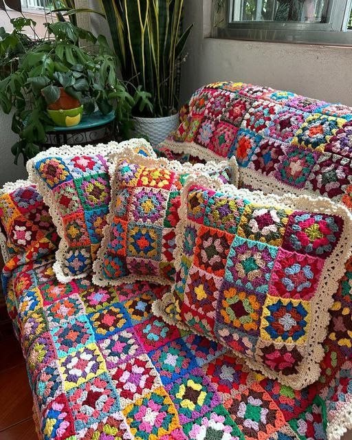 Colorful crochet granny square blankets and pillows on a couch with houseplants nearby