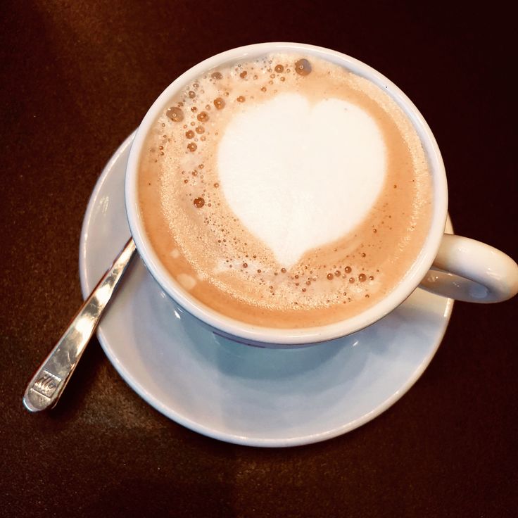 Cappuccino with heart-shaped latte art in white cup on saucer with spoon