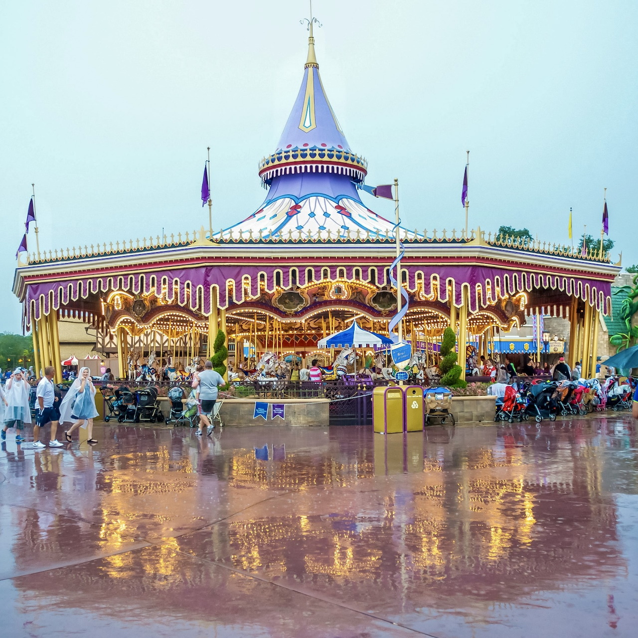 Ornate carousel with painted horses and purple-striped canopy reflecting on wet ground at theme park