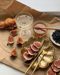 Brunch table with sliced figs, honey bowl, croissants, blackberries, and gold utensils on beige cloth