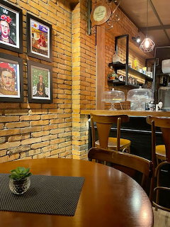 Cozy cafe interior with brick walls, Frida Kahlo portrait art, wooden tables, and a bar counter