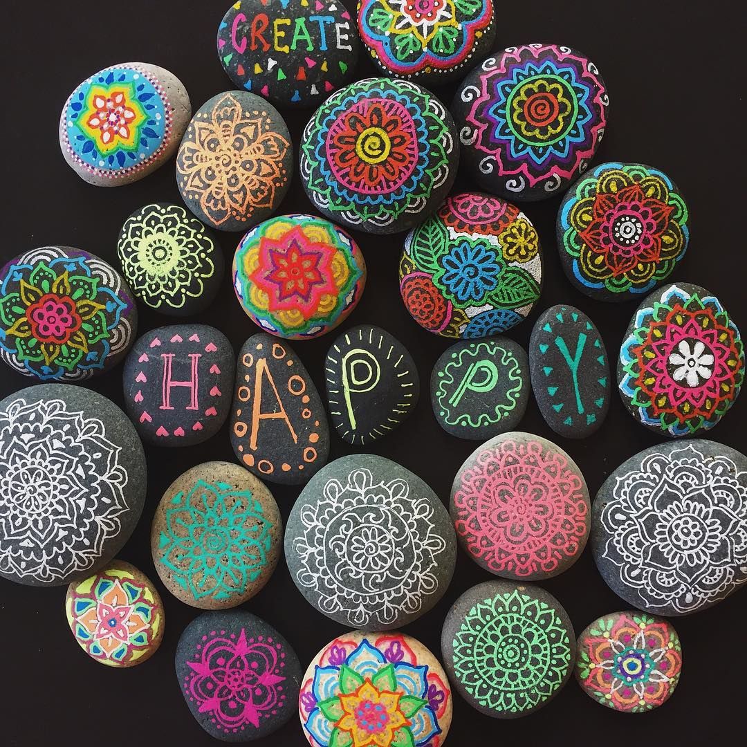Assorted colorful painted stones with mandala and floral patterns on a dark background