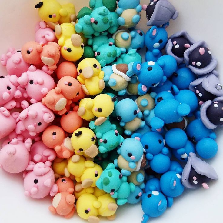 Colorful collection of small polymer clay figurines arranged in a rainbow gradient from pink through yellow to blue