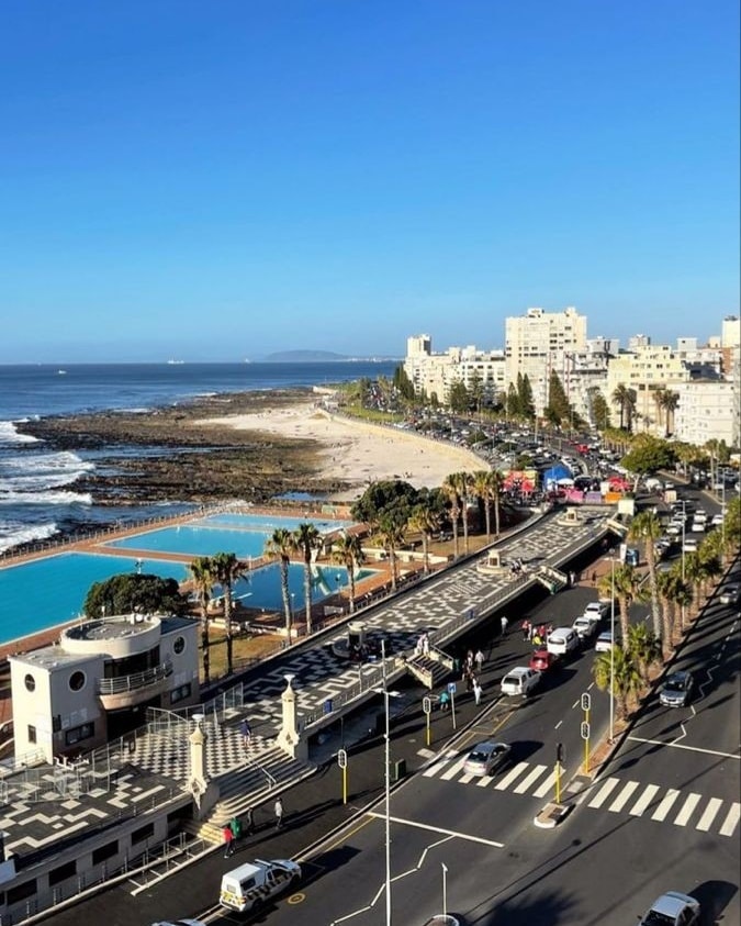 Coastal cityscape with ocean, rocky shoreline, roads, and white buildings under a blue sky