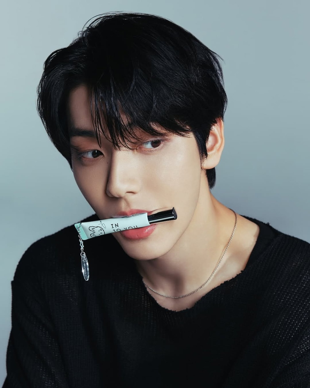 Young Korean man in black sweater holding a small object in his mouth, portrait shot on gray background