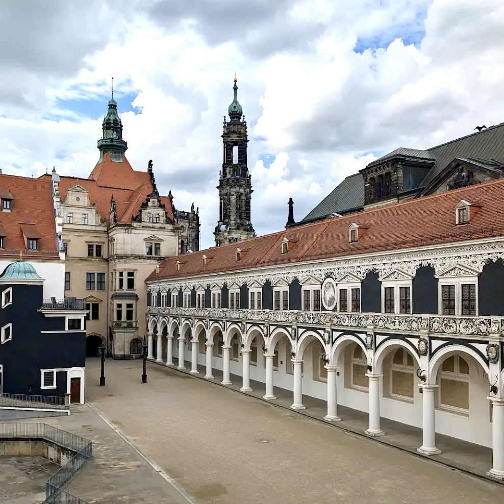Renaissance courtyard with white columned arcade, church spire, and historic buildings under cloudy sky in Dresden