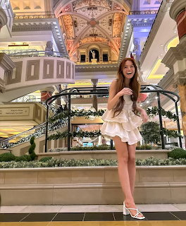 Woman in white dress standing in luxurious hotel lobby with ornate ceiling and grand staircase