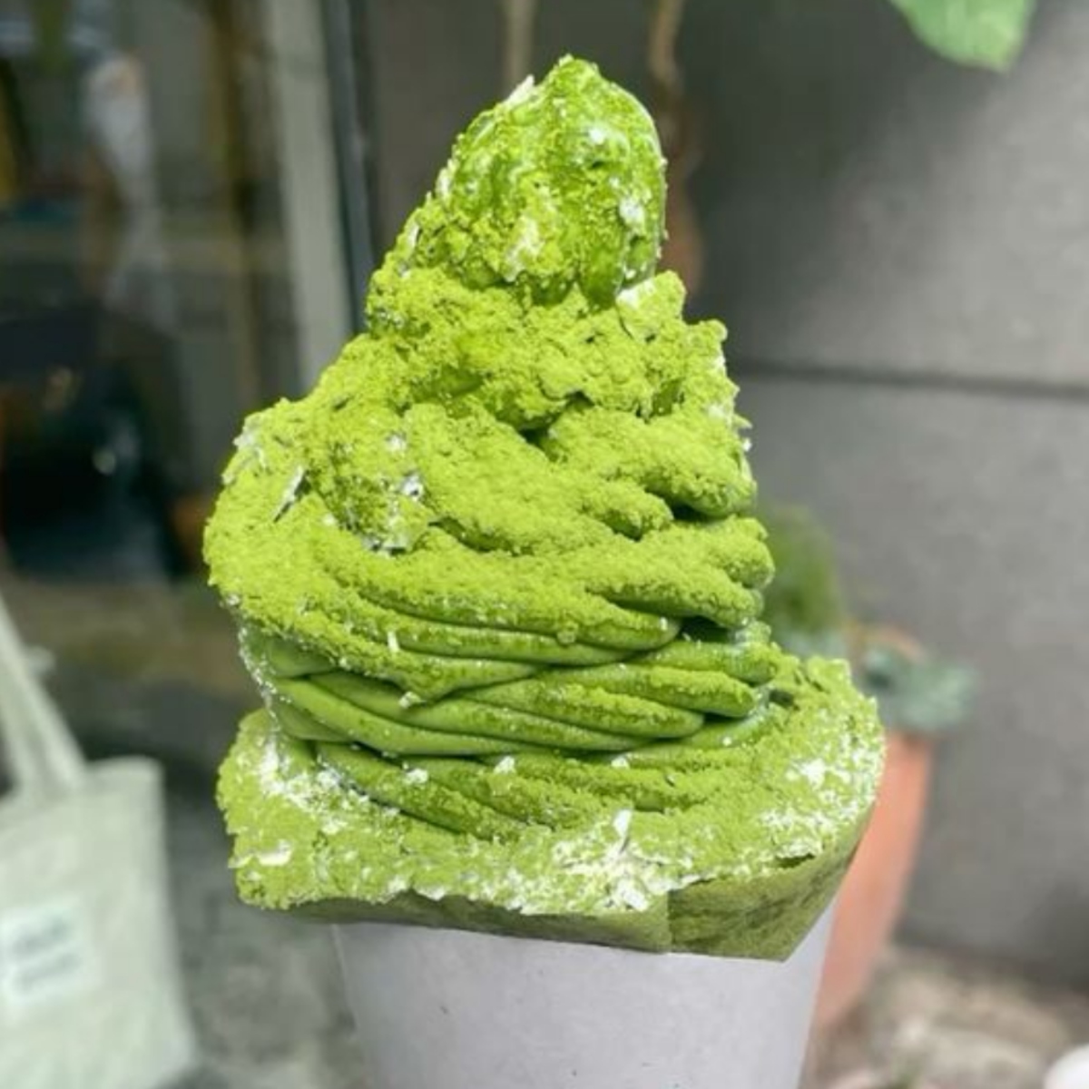Matcha soft serve ice cream in a paper cone with powdered sugar on a green cake base