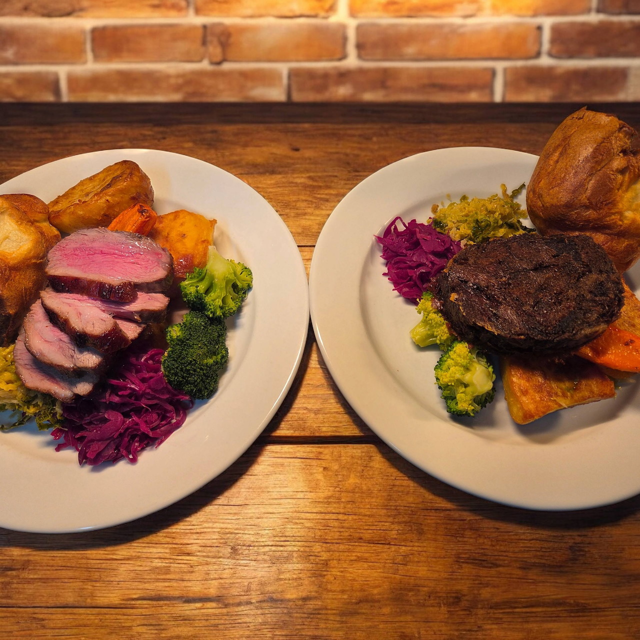 Two plates of roast dinner with beef, Yorkshire pudding, vegetables and gravy on wooden table
