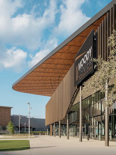 Modern building entrance with angular copper roof, glass walls, and decorative plants