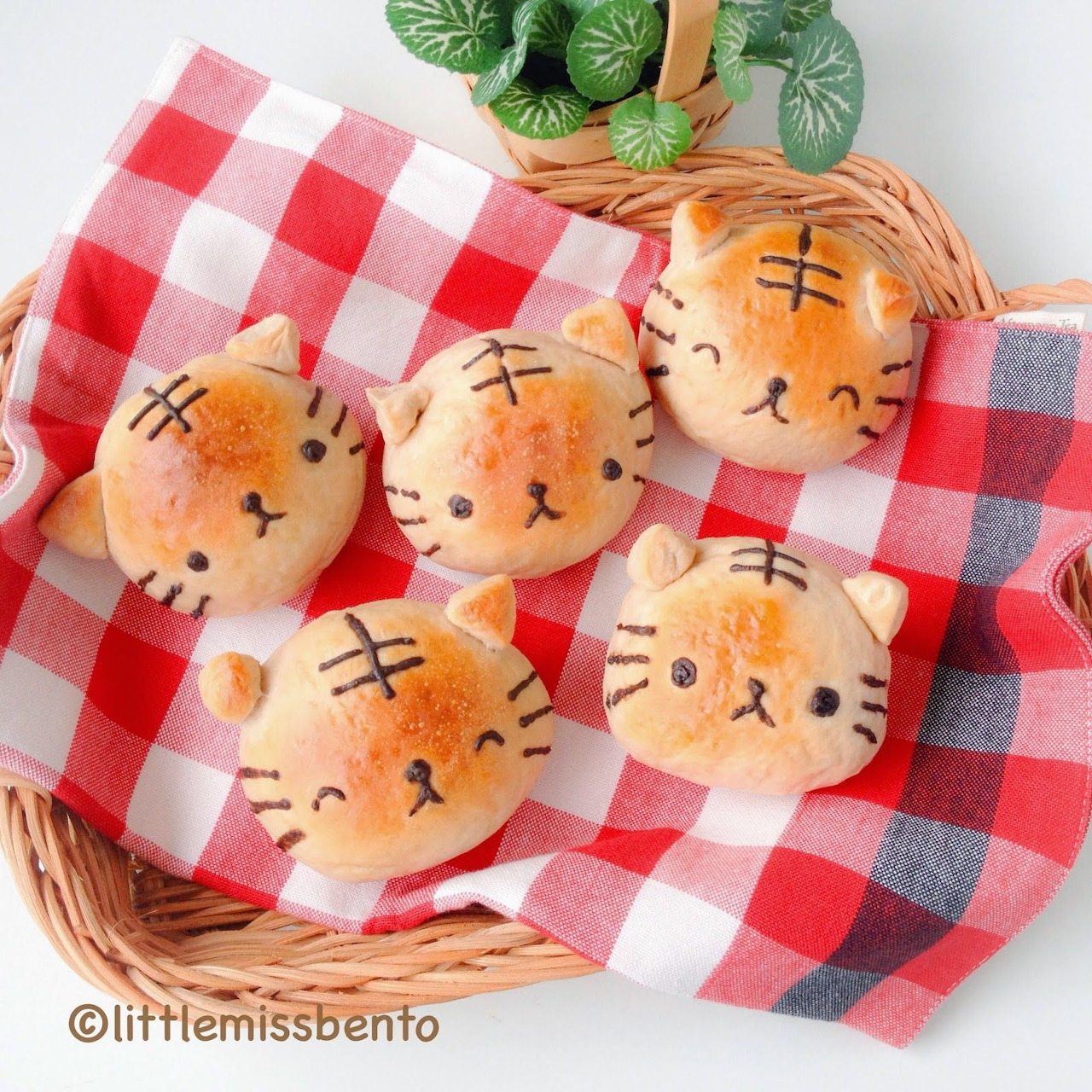 Five tiger-shaped bread buns with striped patterns in a woven basket on red checkered cloth