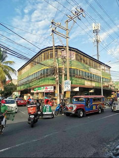 Busy street corner with a market building, tricycles, cars, and power lines