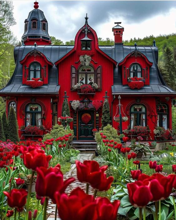 Ornate red Gothic house with pointed gables and garden full of red tulips in the foreground