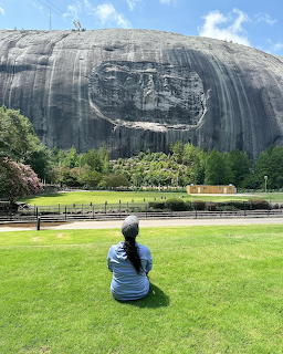 Person sitting on grass looking at the carved face on Stone Mountain