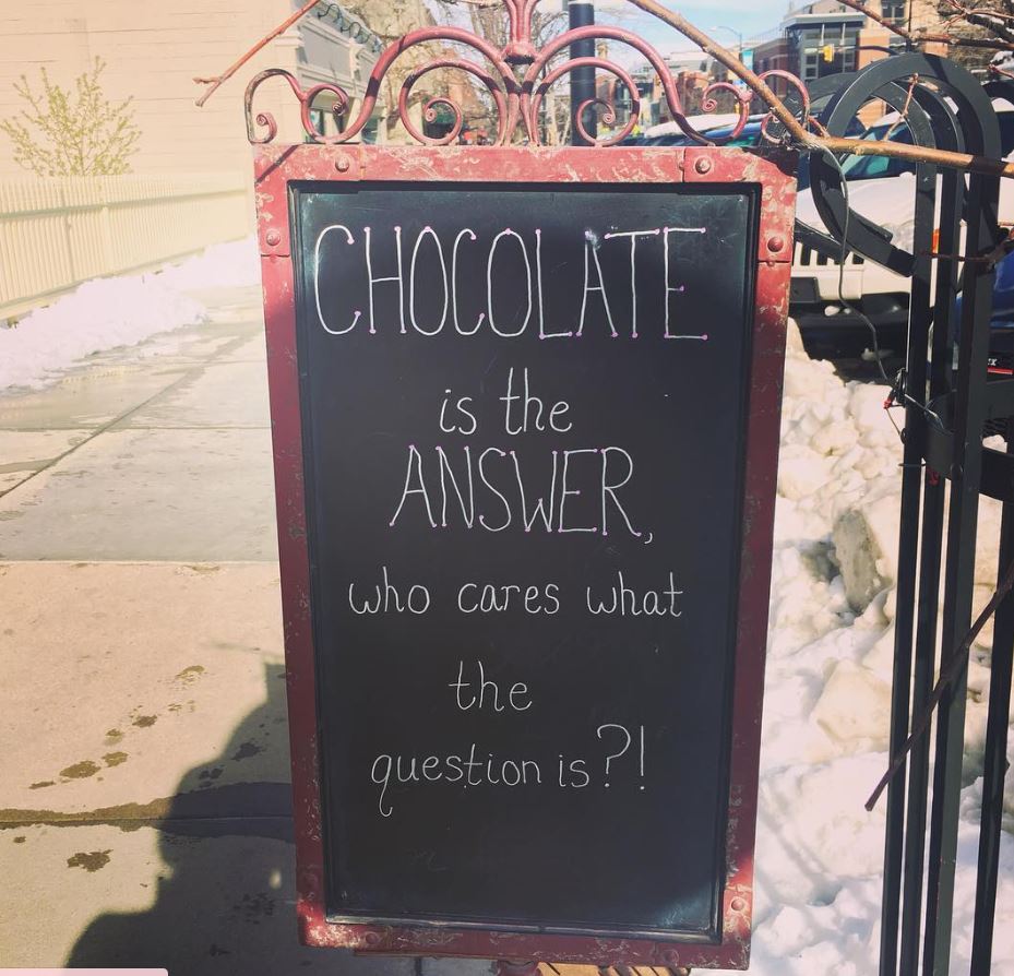 Chalkboard sign outdoors in snow with a handwritten message about chocolate