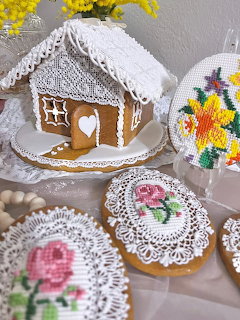 Gingerbread house with white royal icing roof and decorated cookies with embroidered floral designs