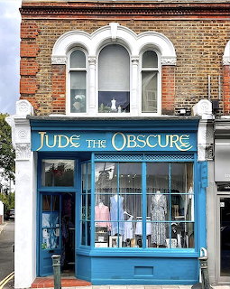 Blue storefront of Jude the Obscure vintage clothing shop with display windows and brick Victorian building above