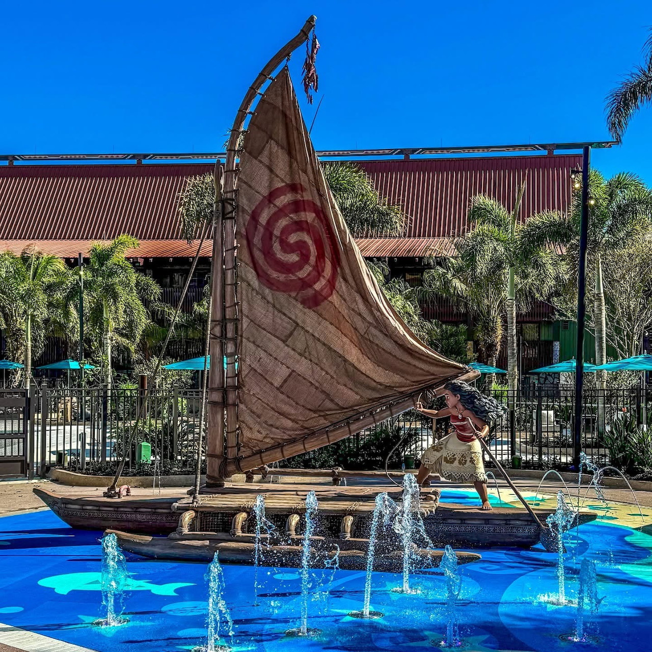 Polynesian outrigger canoe with red spiral sail in resort fountain