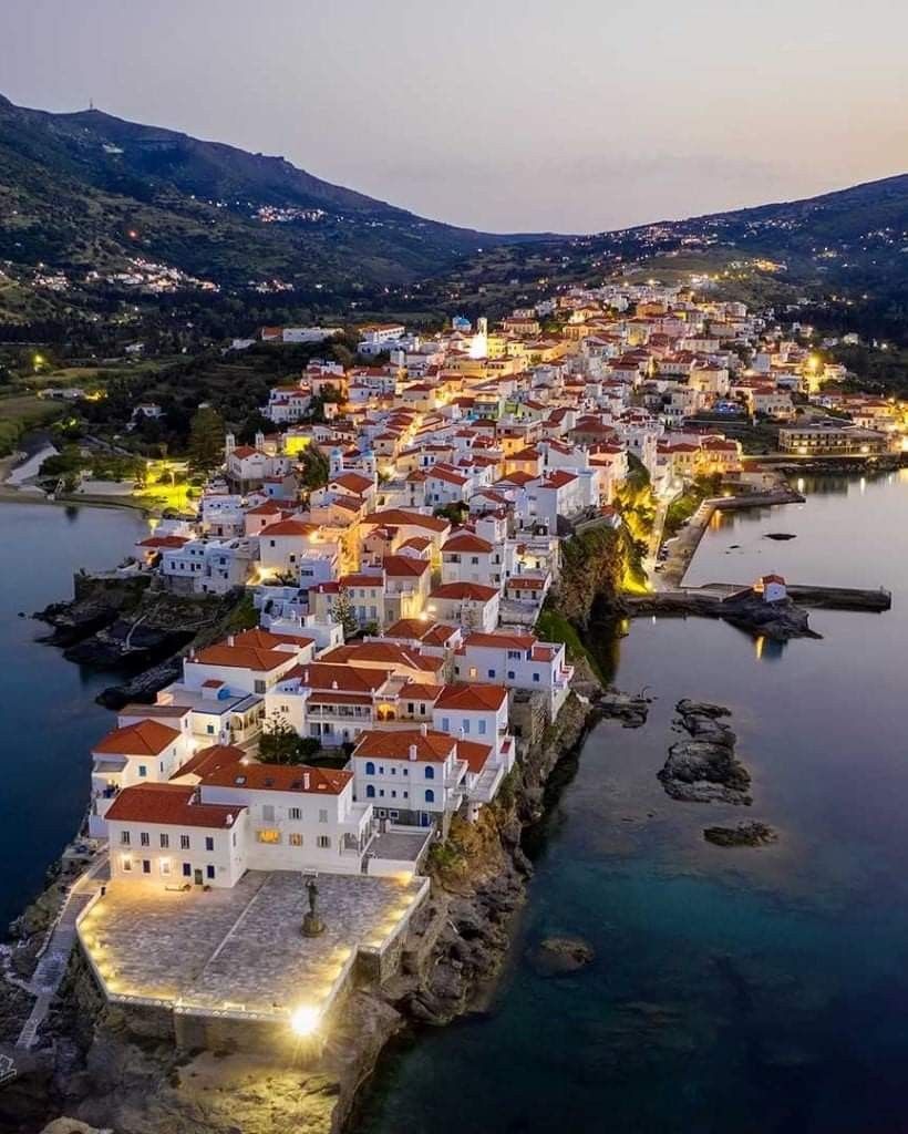 Aerial dusk view of Andros island, Greece, white buildings with red roofs on rocky coastline