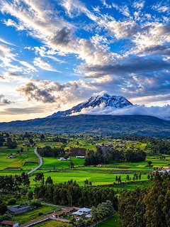 Snow-capped Chimborazo mountain above green farmland under a dramatic cloudy blue sky