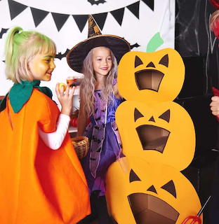 Three children in Halloween costumes at party with pumpkin decoration and bunting