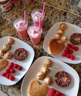 Overhead view of donuts, cookies, raspberries, and pink drinks with whipped cream on white plates