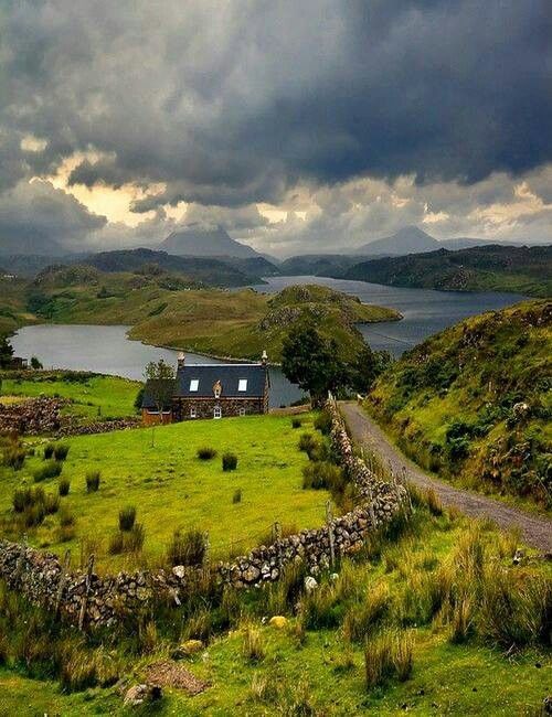 Abandoned stone cottage with loch and mountains under stormy sky in Scottish Highlands