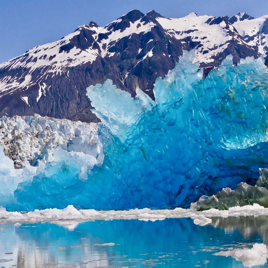 Bright blue glacier ice formations in mountain lake with snowy peaks