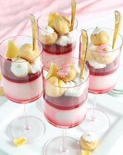 Four layered panna cotta desserts in glasses with pink jelly, cream, cookies and flowers
