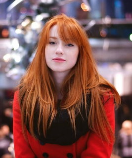 Portrait of a young redhead woman with long hair, wearing red and black, with bokeh lights behind her