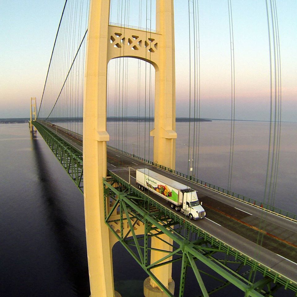 Yellow suspension bridge with vehicle crossing at dusk over calm water