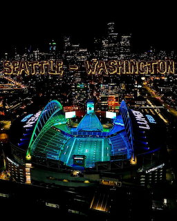 Aerial night view of Lumen Field stadium in Seattle lit up in green and blue with city buildings behind