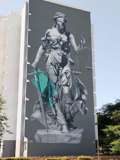 Street art mural of Lady Justice holding scales and sword on the side of a building