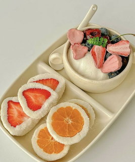 Dessert tray with fruit topped cream rounds and berry bowl with pink macarons